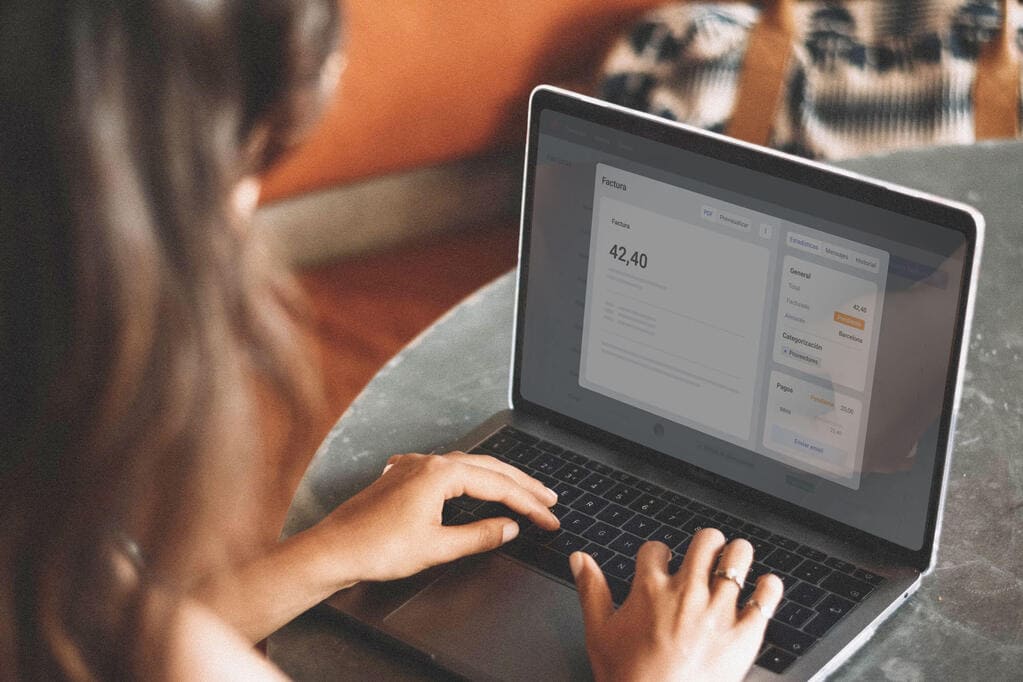 Una mujer usa un portátil. Se le ve de lado y sus manos sobre el teclado. La pantalla muestra una aplicación de finanzas, con la cifra 42,40